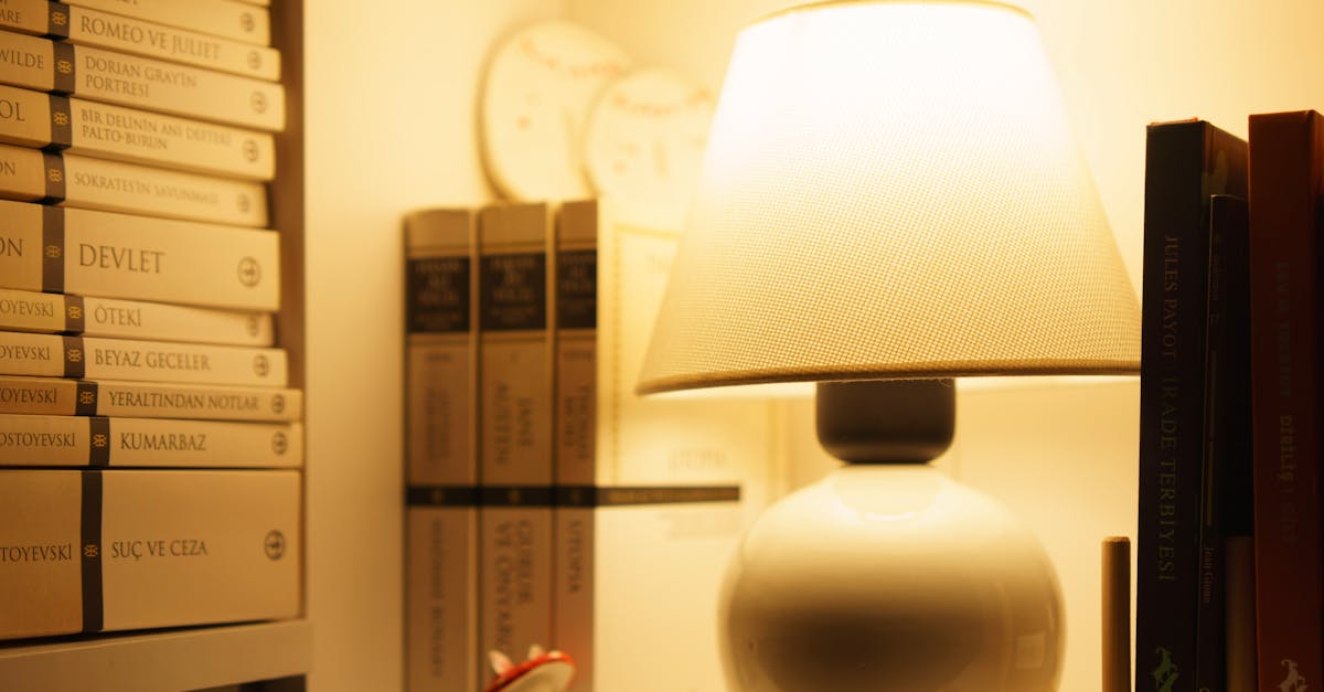 A warmly lit bookshelf with stacked books and an elegant table lamp, creating a cozy reading atmosphere.
