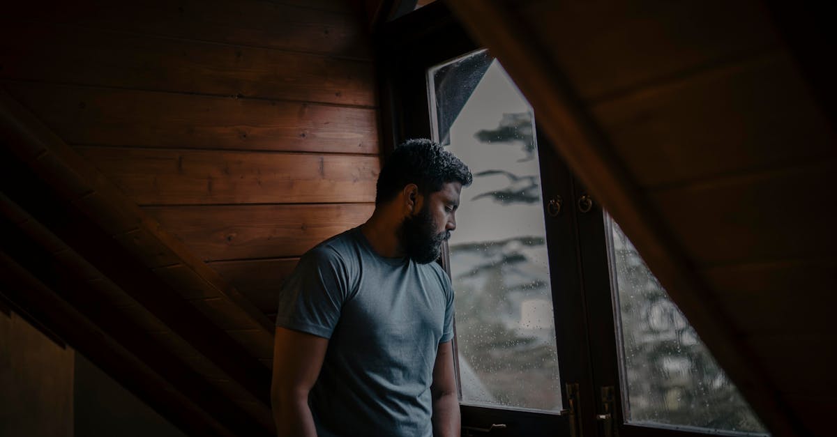 A thoughtful man stands by a window, lost in contemplation, indoors in Sri Lanka.