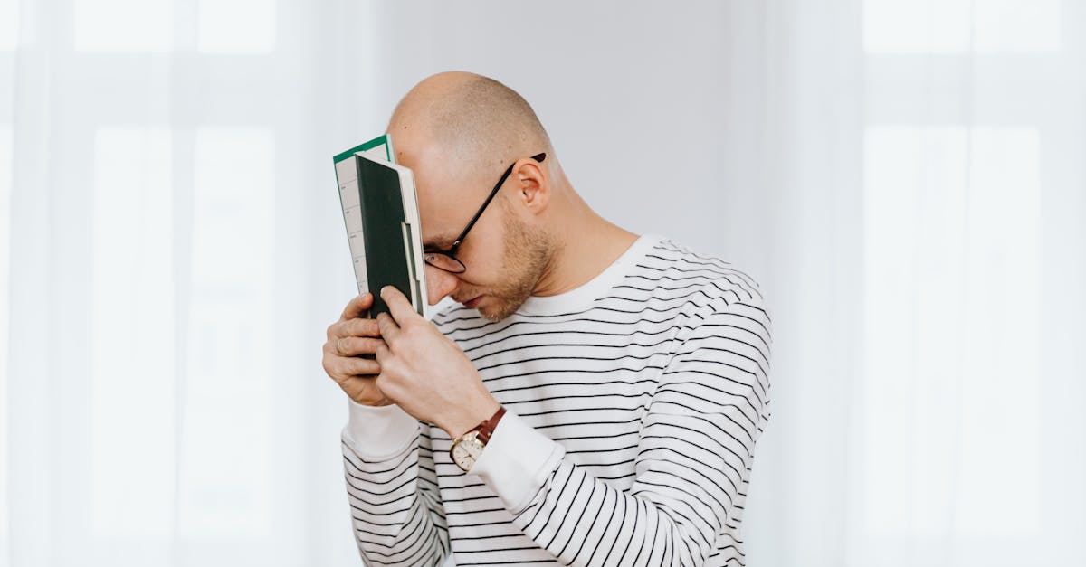 Bald man with eyeglasses in striped shirt holding a notebook indoors.