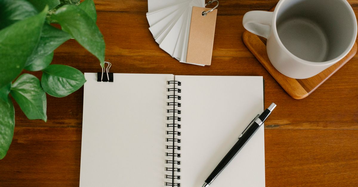 From above empty notebook with pen and tags placed near potted plant and empty mug on office table
