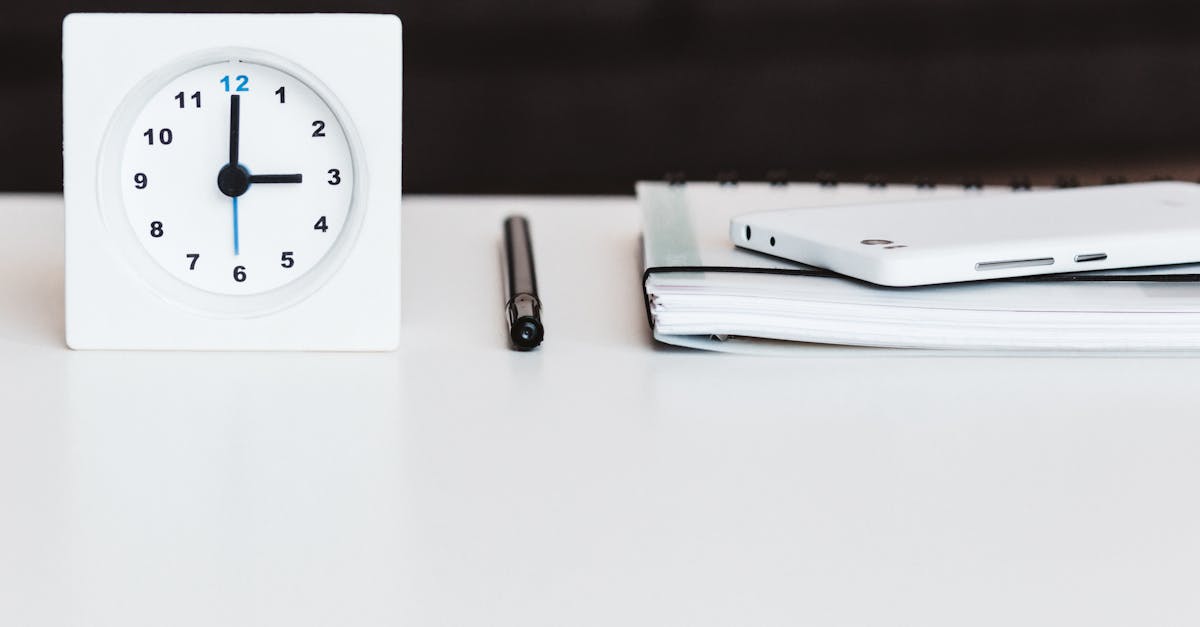 A minimalist office desk setup with a clock, pen, smartphone, and notebook, conveying time management and orga