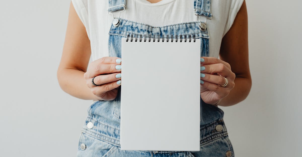 A woman in denim overalls holding a blank notepad, ideal for creative mockup use.
