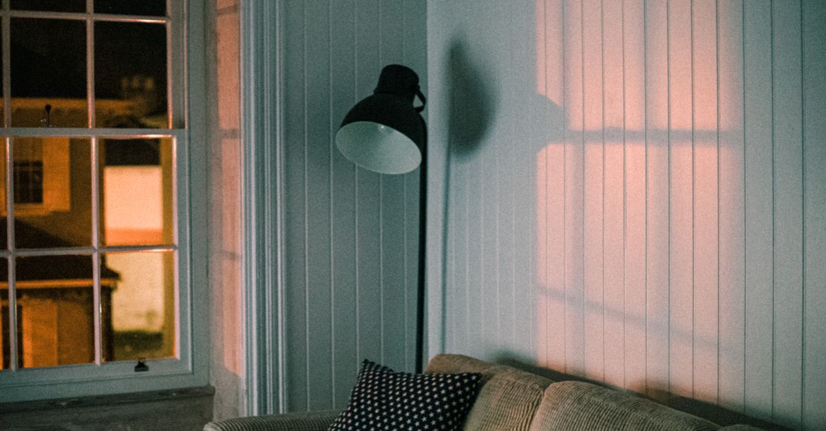 A warm and inviting living room featuring a soft couch and floor lamp casting shadows on the wall.