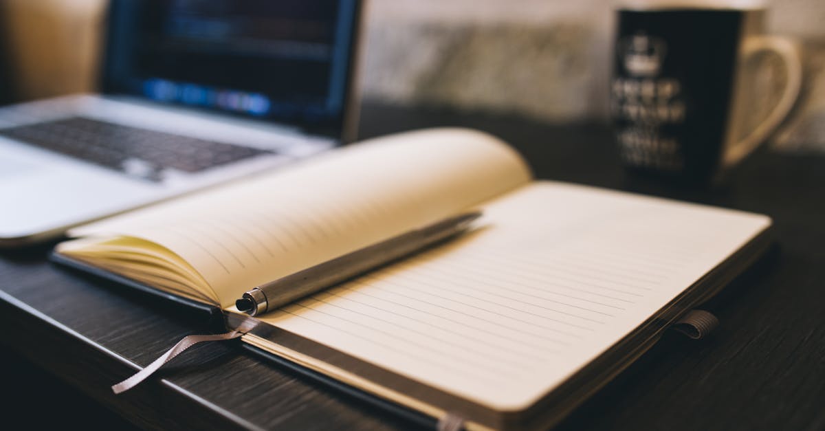 Open notebook with a pen on a wooden desk beside a laptop, ideal for blogging and work-related themes.