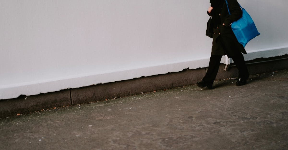 A woman carrying a blue bag walks along a concrete sidewalk, captured in a candid urban scene.