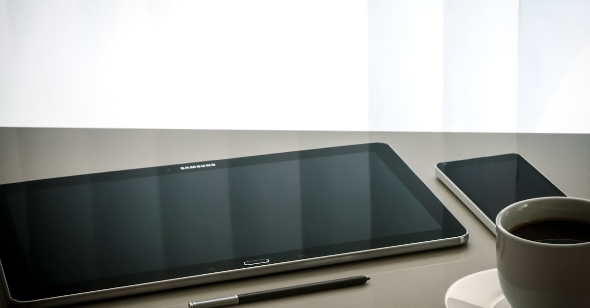 Minimalist office desk setup featuring a tablet, smartphone, pen, and coffee cup on a reflective surface.