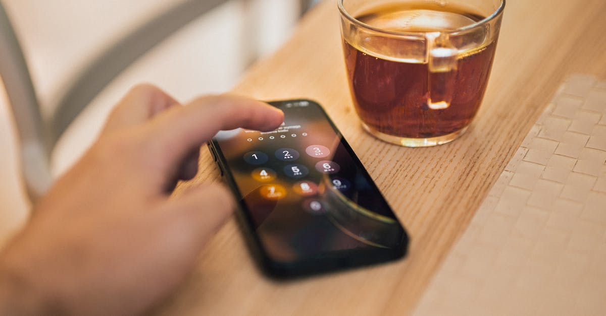 Close-up of hand unlocking a smartphone next to a cup of tea on a wooden table, emphasizing technology and sec