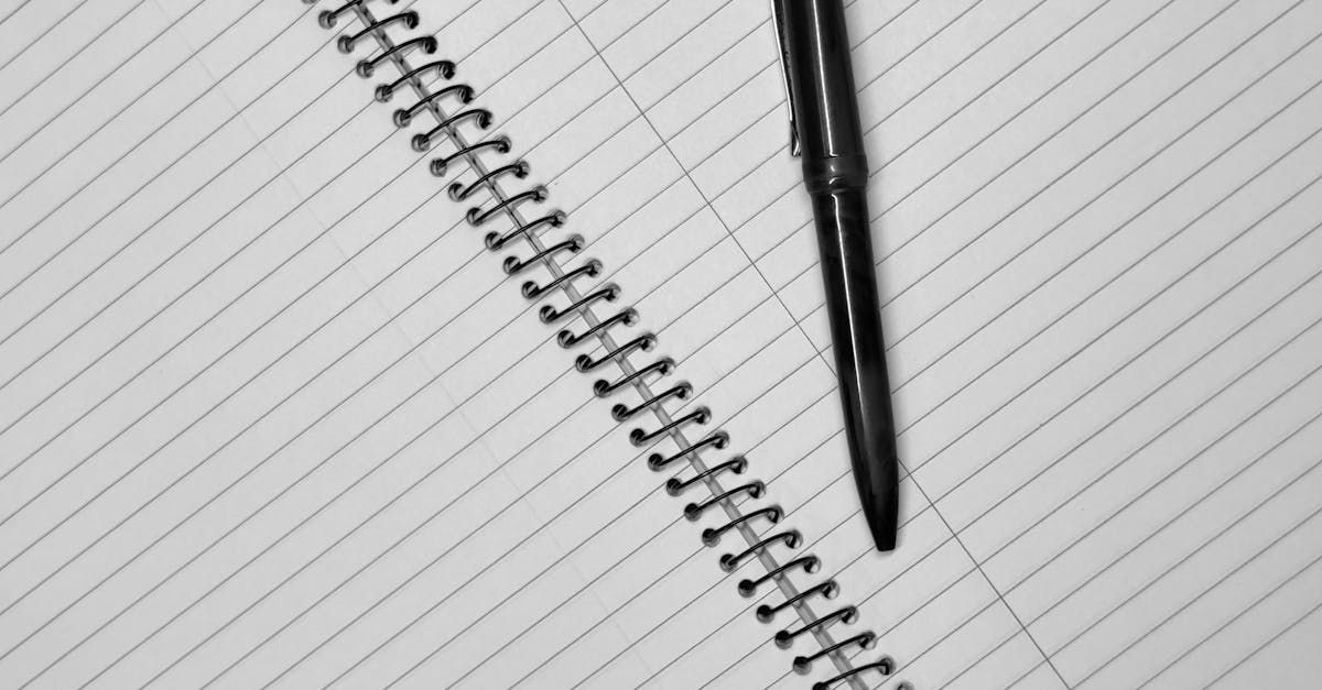 Close-up of a black pen resting on an open spiral notebook with lined pages.