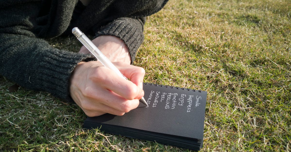 Close-up of a person writing emotions in a notebook while lying on grass outdoors.