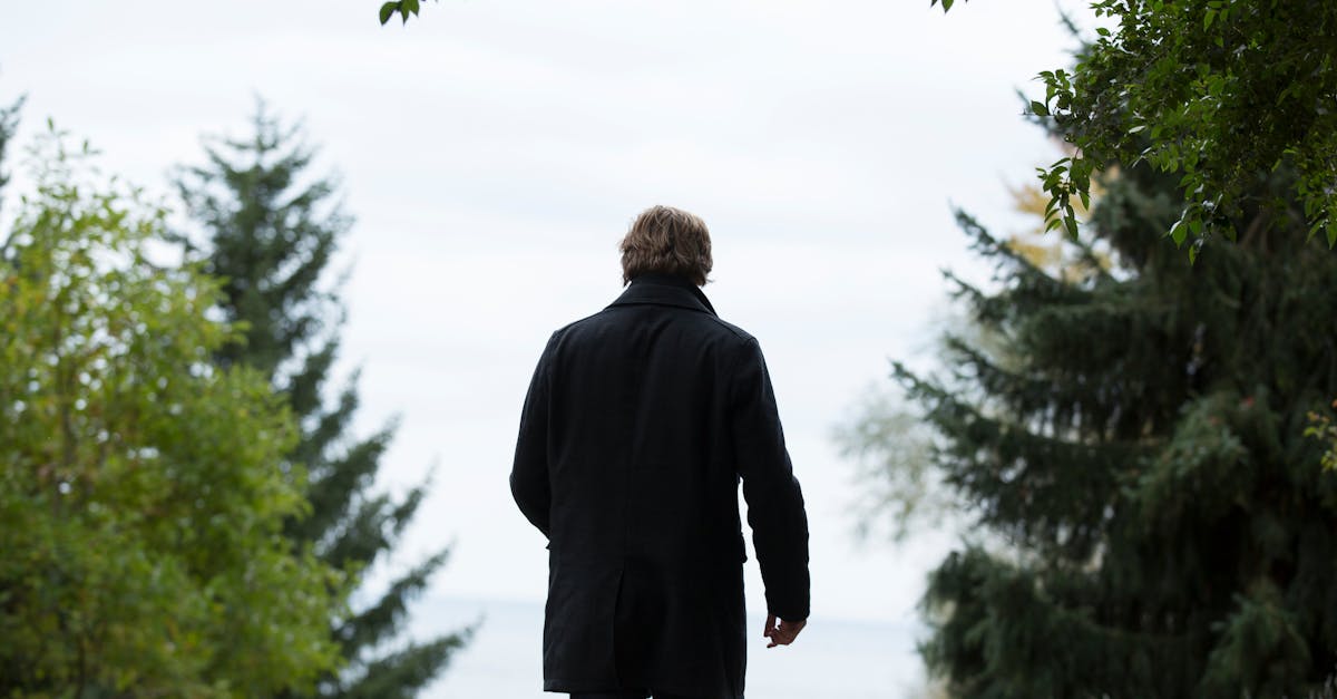 A lone man walks through a peaceful forest path, surrounded by trees and greenery, towards the ocean.