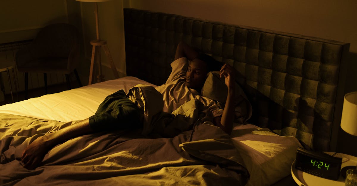 A restless man lying awake on his bed in a dimly lit bedroom at night.