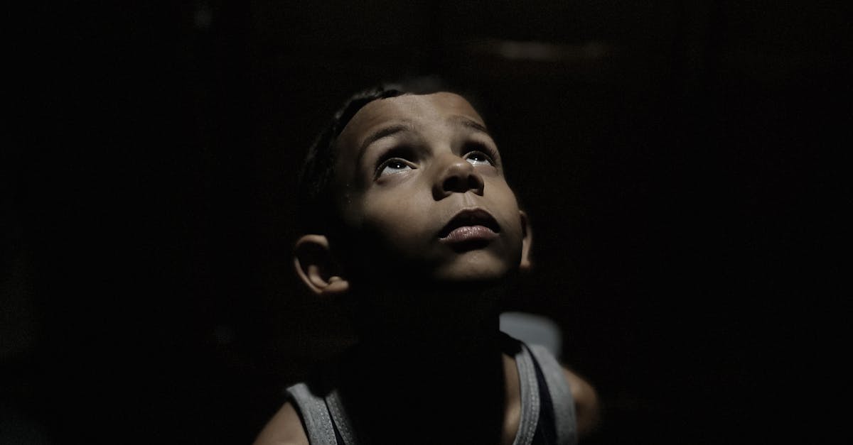 Portrait of a child looking up, seemingly contemplative, in a dimly lit environment.