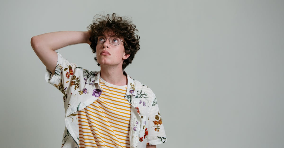 A young man with curly hair and glasses thinking in a studio setting.