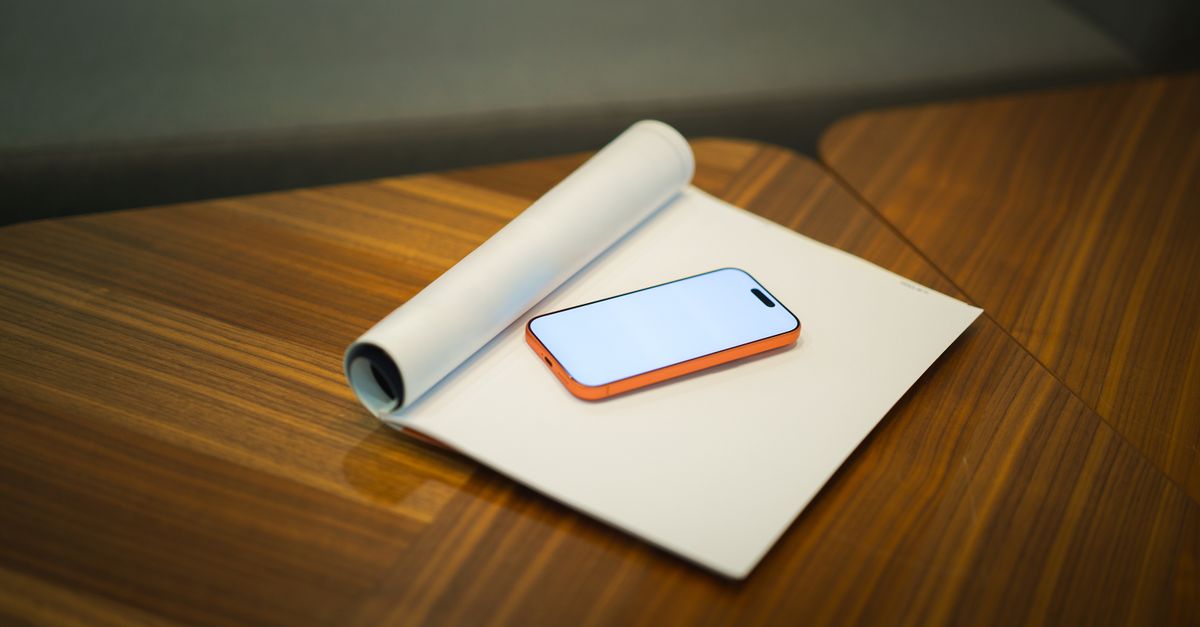 Modern workspace featuring a smartphone and roll of paper on a wooden desk, ideal for office presentations.