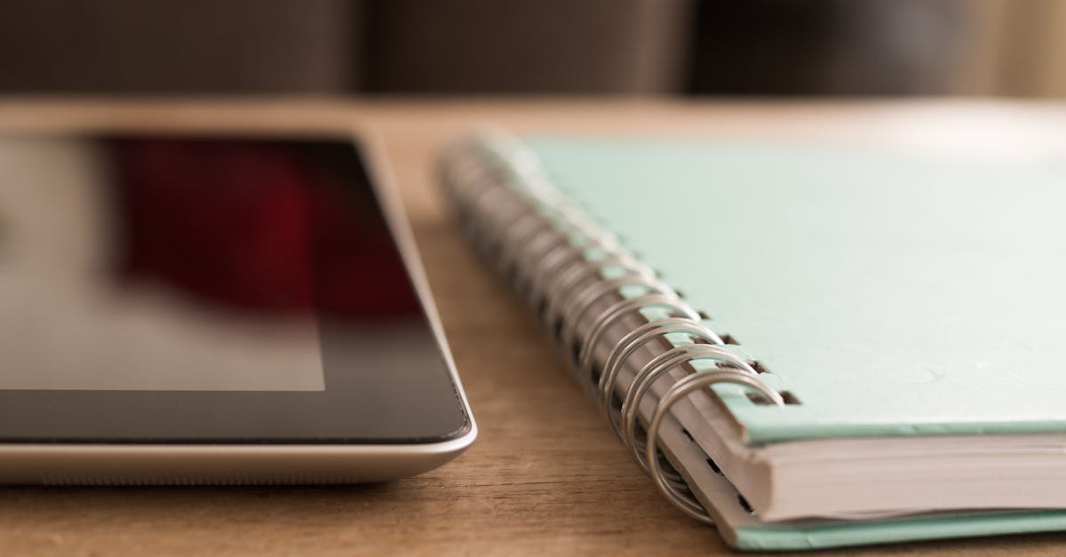 A close-up photo of a tablet alongside a spiral notebook on a wooden desk.