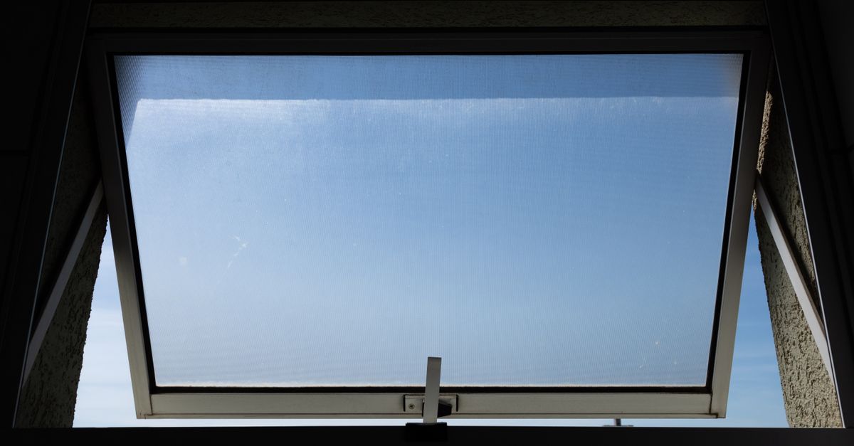A low angle view of an open skylight window revealing a clear blue sky.