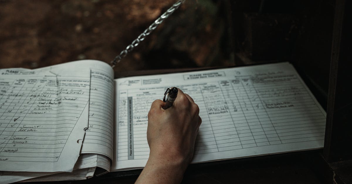 Close-up of a person writing in an outdoor logbook on a table.