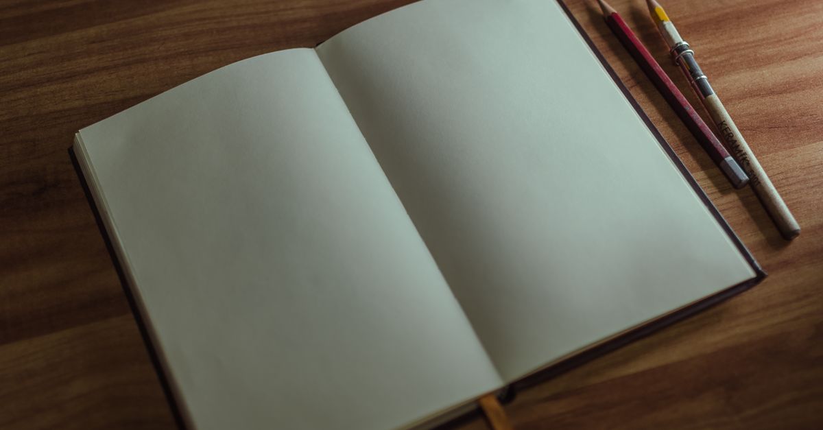 An open sketchbook with pencils on a wooden desk, perfect for artists and creatives.