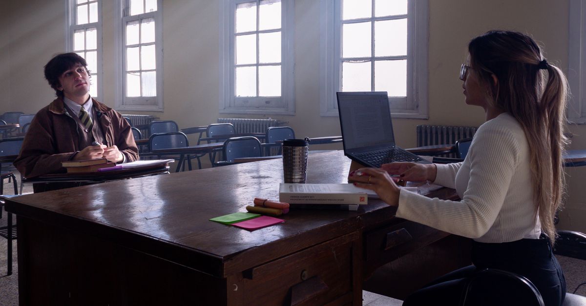 Two young adults studying in a sunlit classroom with laptops and notebooks.