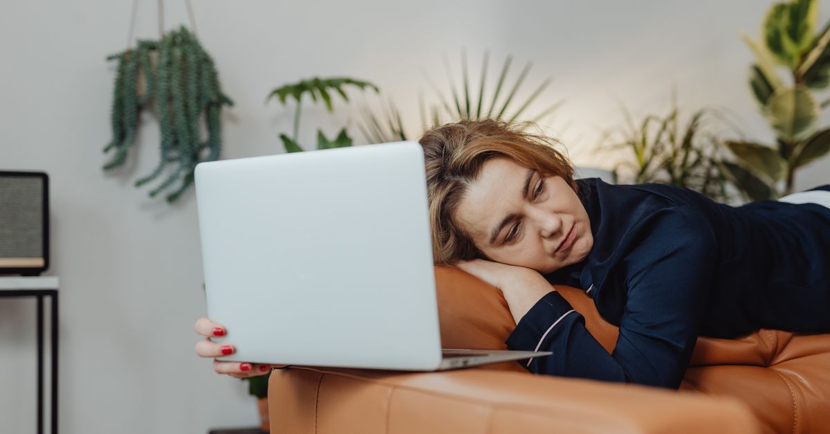 A woman working on a laptop with a glass of wine in a dimly lit room.