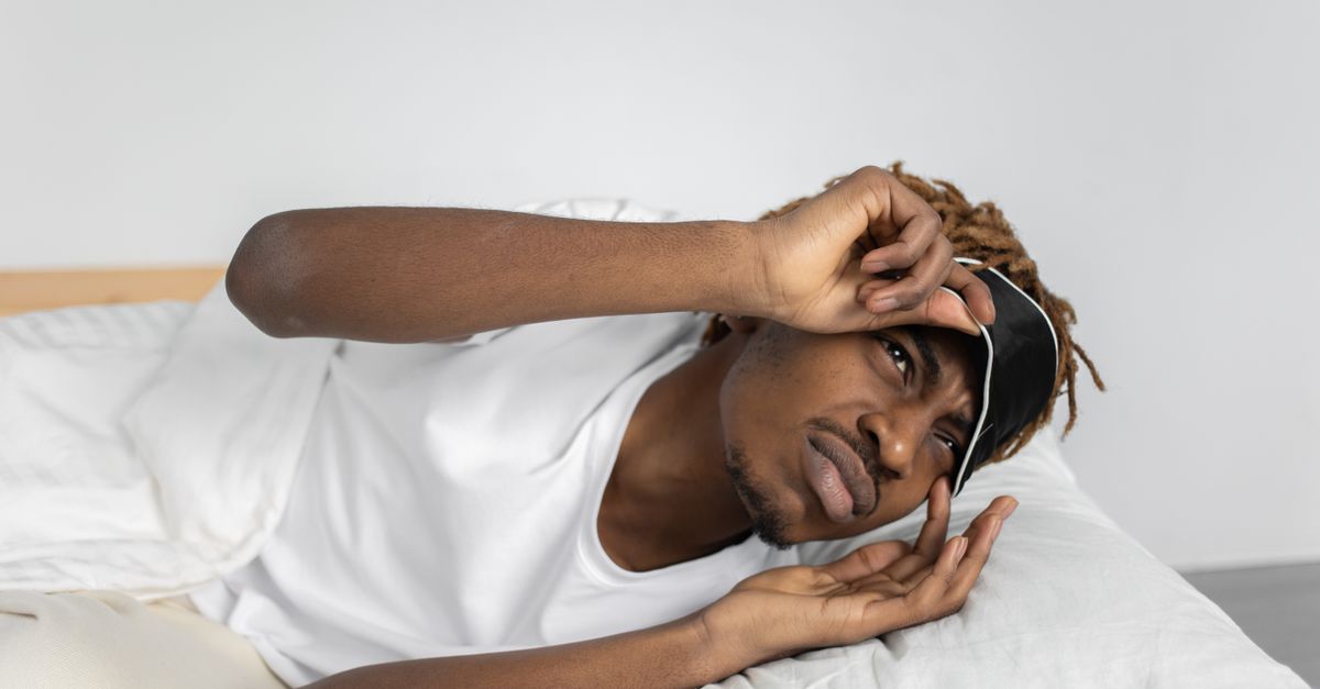 Young man removes sleep mask, starting his day in bed, indoors.