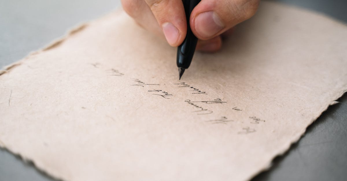 A close-up view of a person's hand writing with a black pen on textured paper.