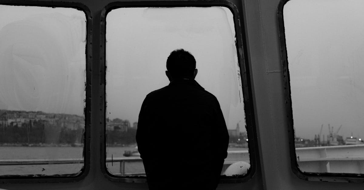Black and white silhouette of a person looking out of a ship window at sea.