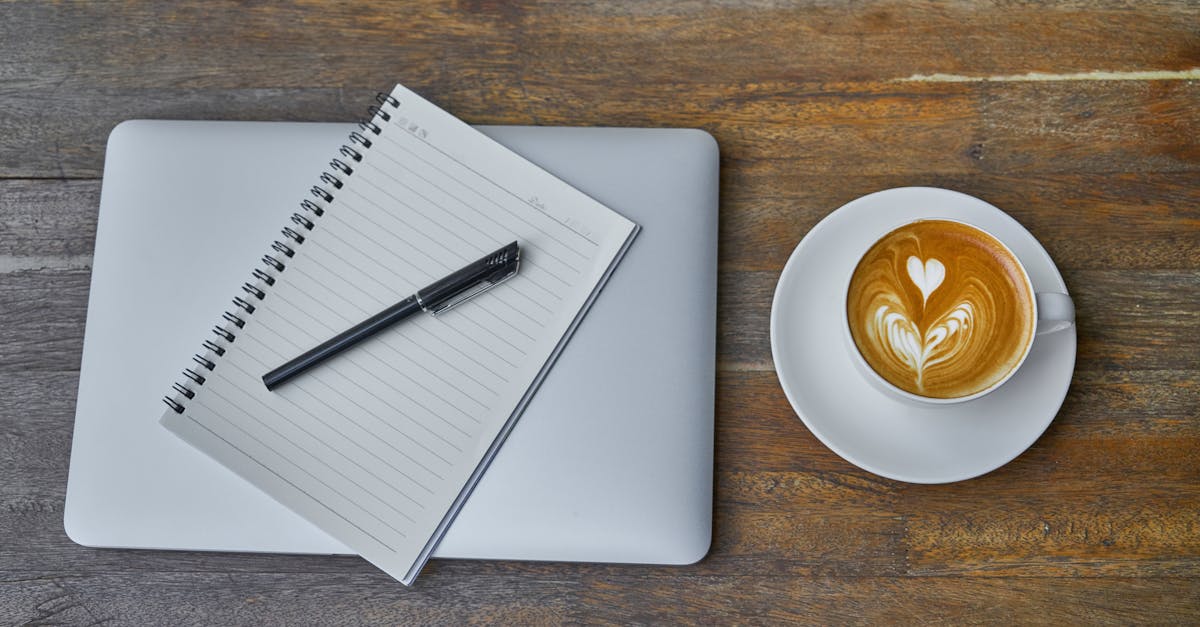 Flat lay of a coffee cup, notebook, pen, and laptop on a rustic wooden table.