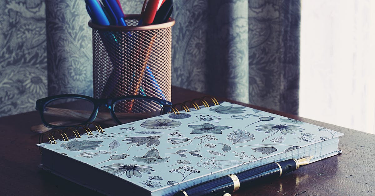 A stylish workspace featuring a floral notebook, glasses, and pens on a wooden desk.