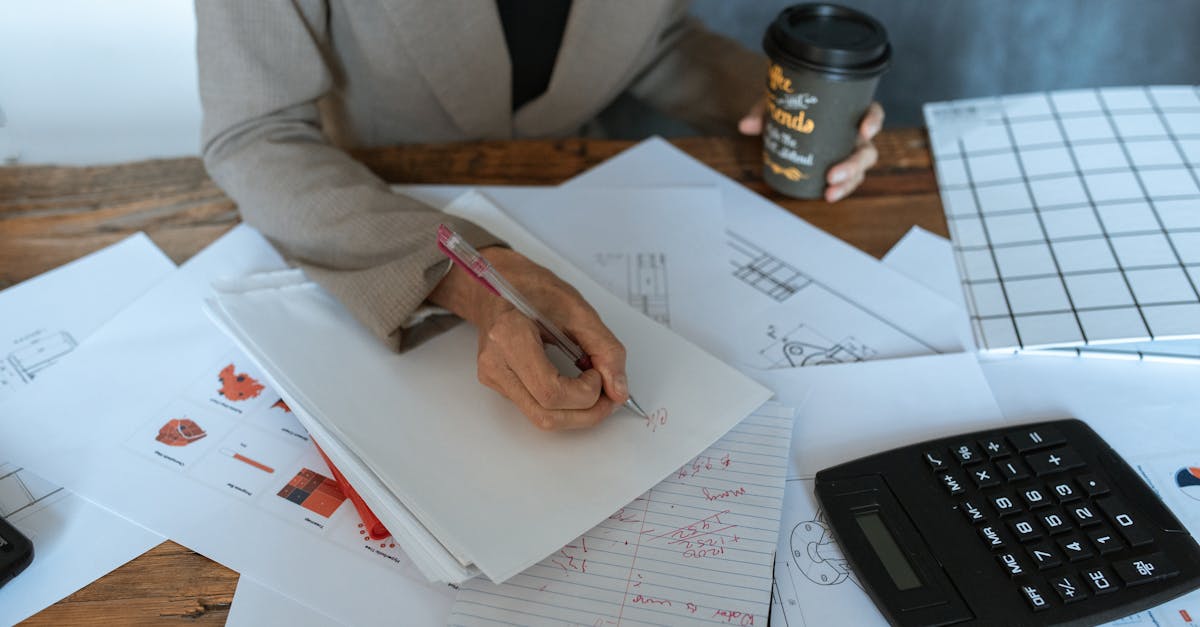 Close-up of a person writing at an office desk with documents and coffee, symbolizing productivity.