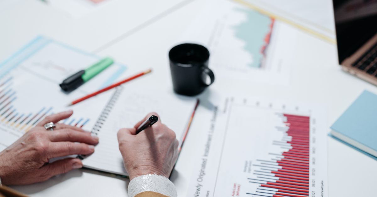 Close-up of hands writing in a notebook surrounded by business charts and documents.