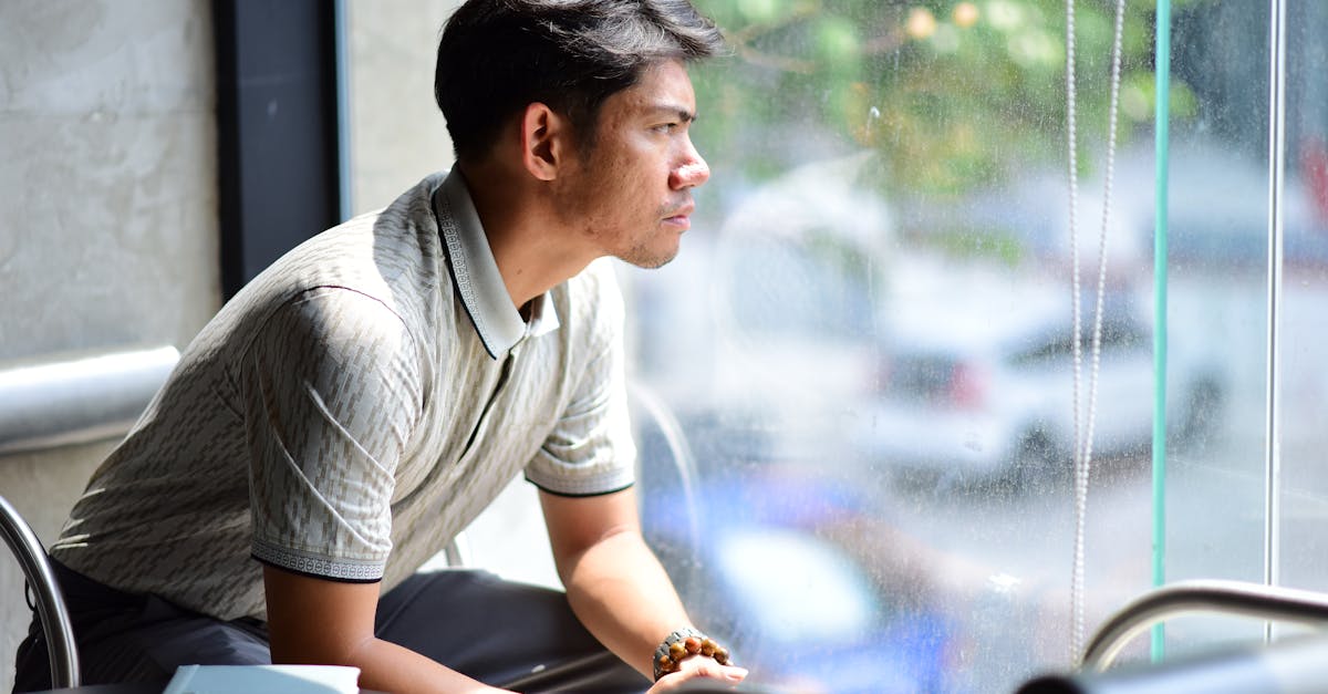 Man sitting by a window in a café, gazing outside in contemplation under soft daylight.