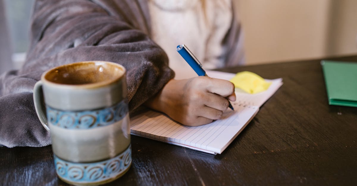 A person comfortably writing in a notebook while enjoying a cup of coffee indoors.