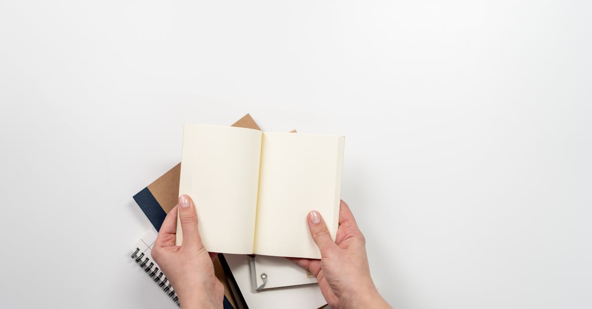 Hands holding an open blank notebook above a stack of stationery items on a desk, perfect for planning concept