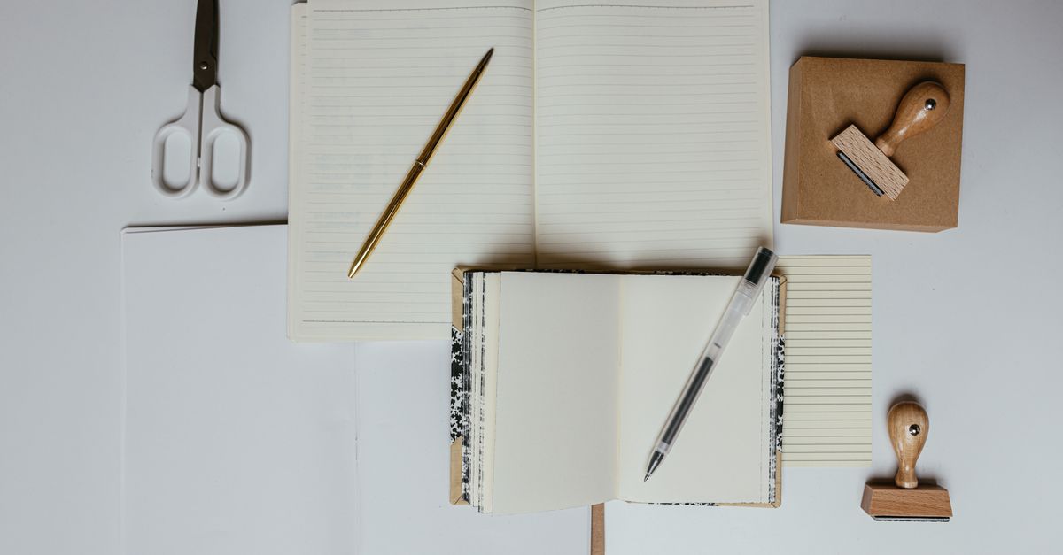 Flat lay of stationery including notebooks, pens, scissors, and stamps on a desk. Ideal for office or school t