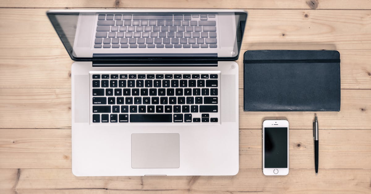 A neatly organized workspace featuring a laptop, smartphone, notebook, pen, and planner on a glass table.