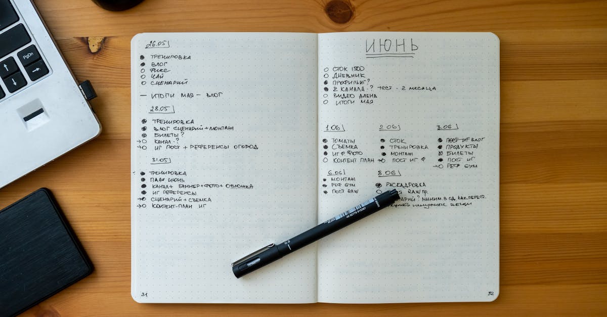 An open notebook with handwritten notes resting on a wooden desk beside a laptop and pen.