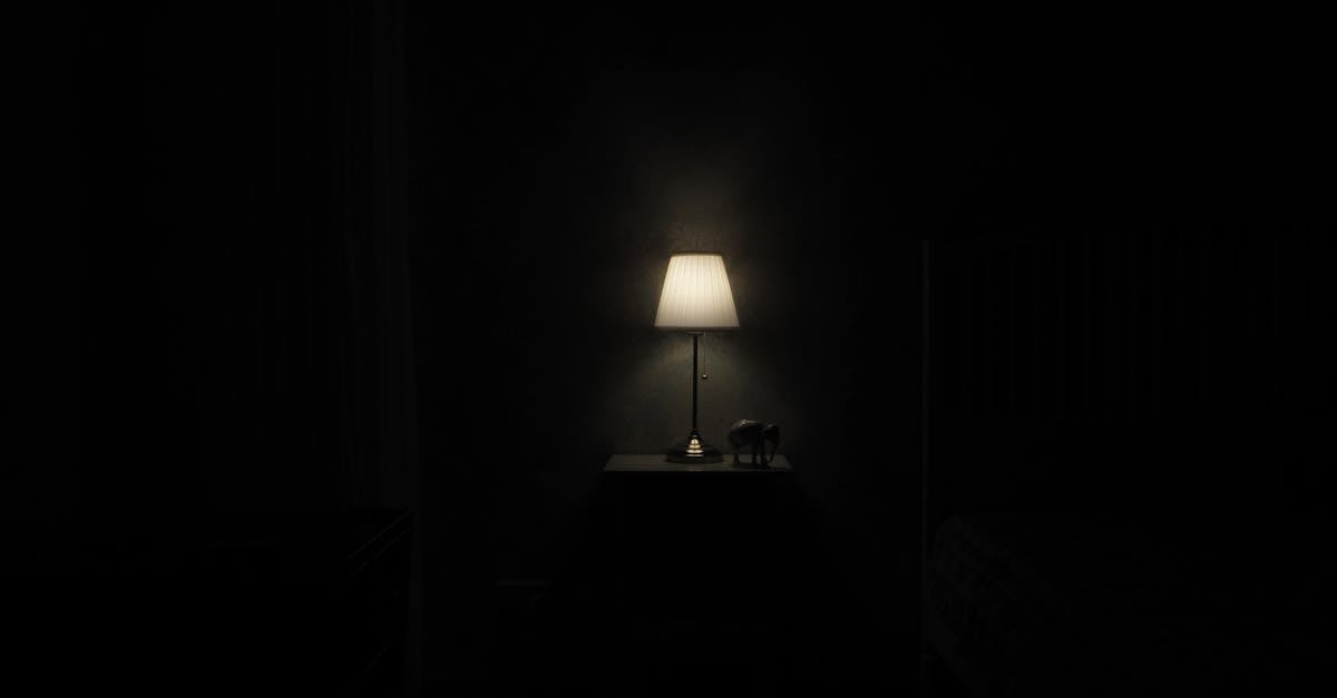Illuminated lamp on nightstand casting a warm glow in a dark, minimalist room.