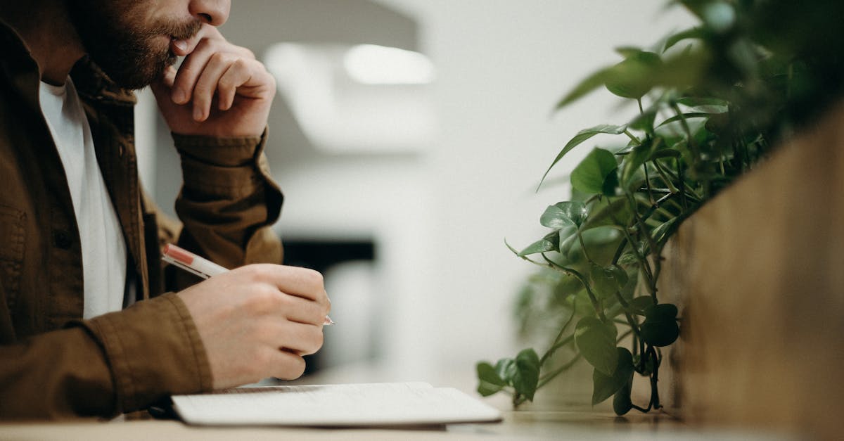 A man deeply concentrates while writing in an indoor office with plants.