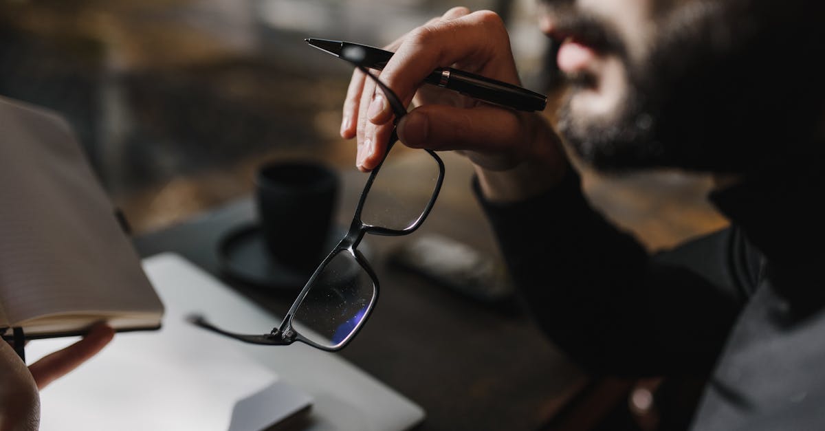 A close-up of a person holding eyeglasses and a pen, with a focus on contemplation.